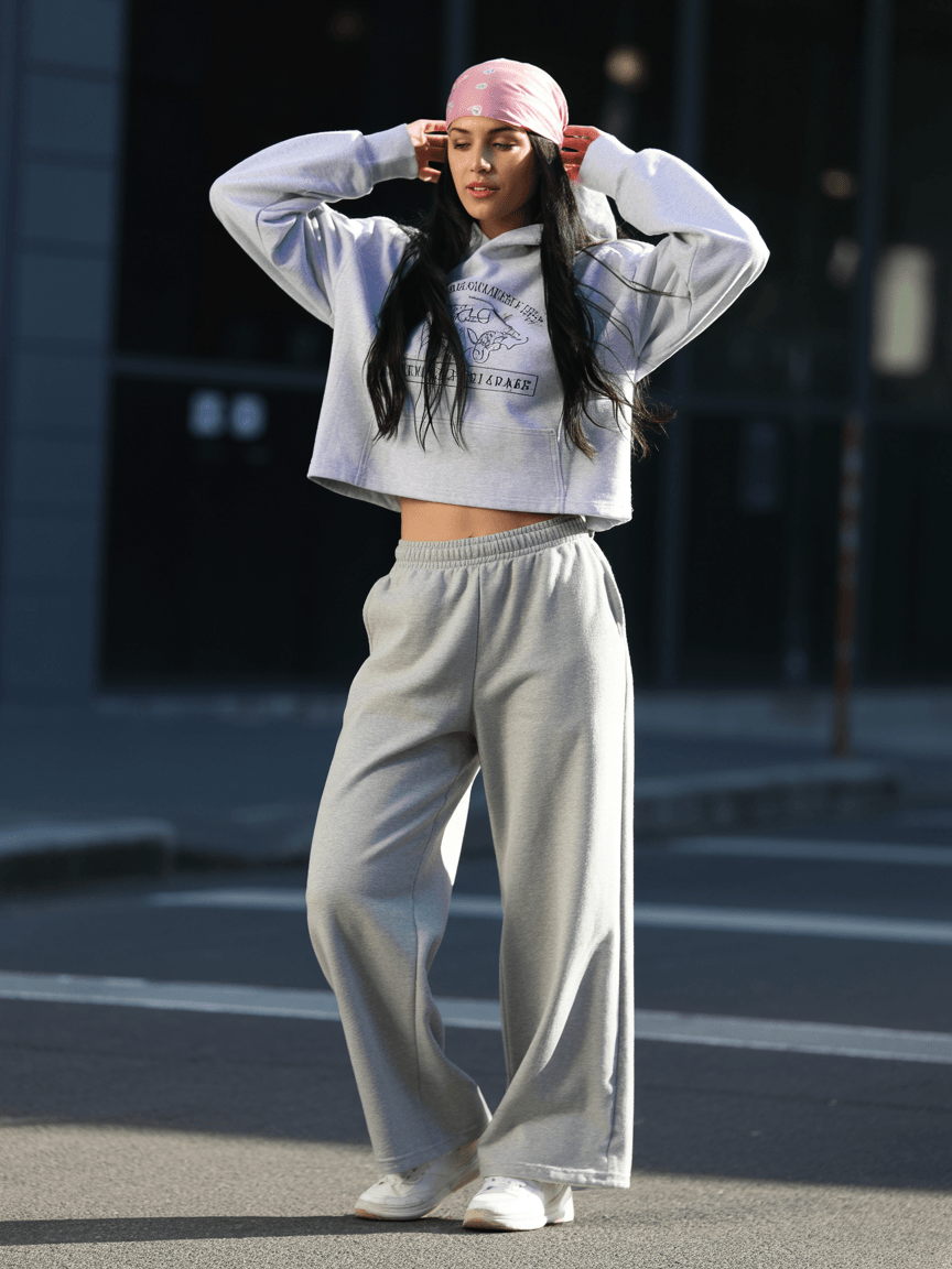 Cropped Grey Hoodie With Printed Logo, Paired With Wide-Leg Grey Sweatpants, White Sneakers, And A Pink Bandana.